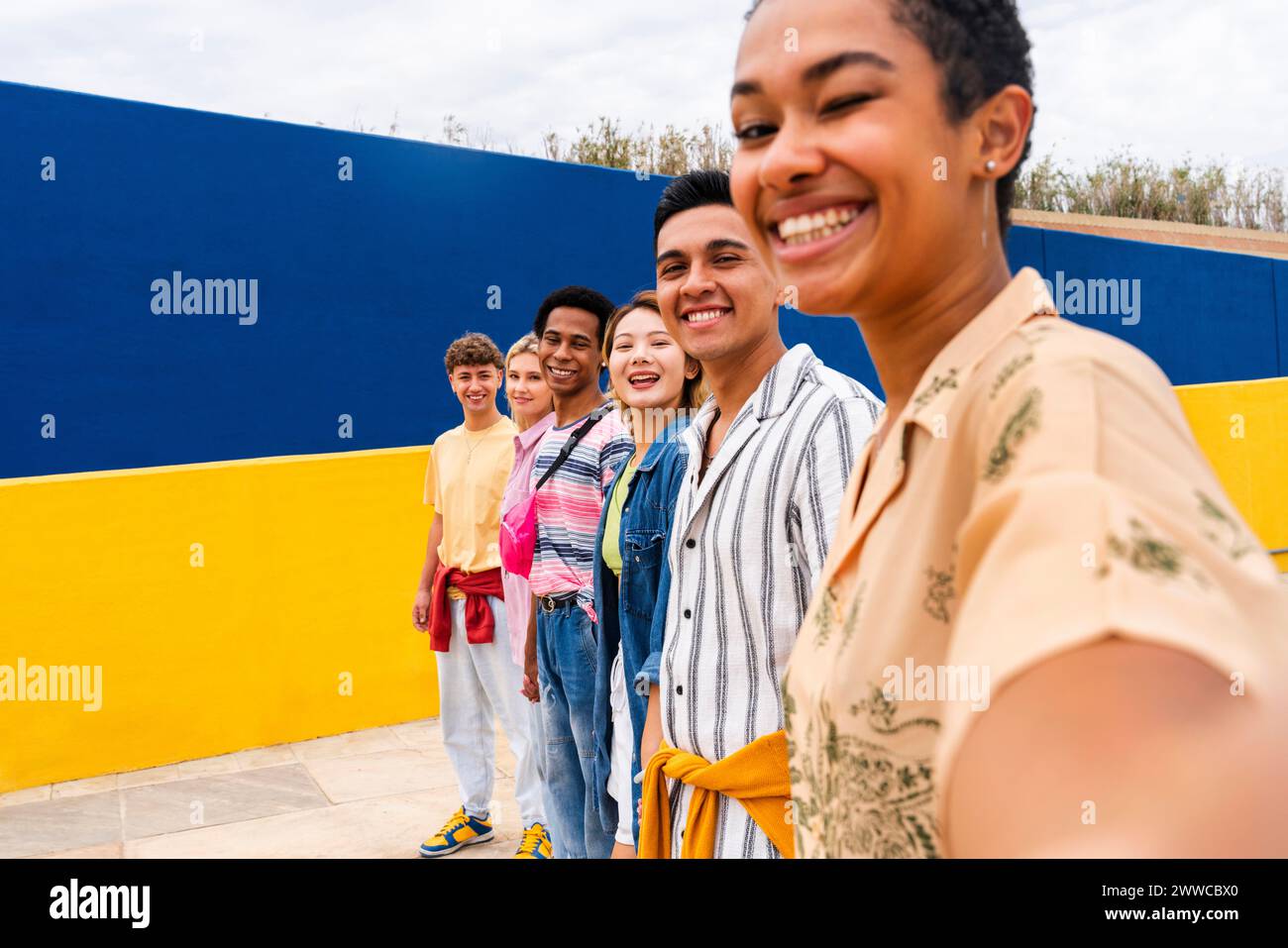 Groupe multi-ethnique de jeunes amis debout souriant devant un mur coloré Banque D'Images