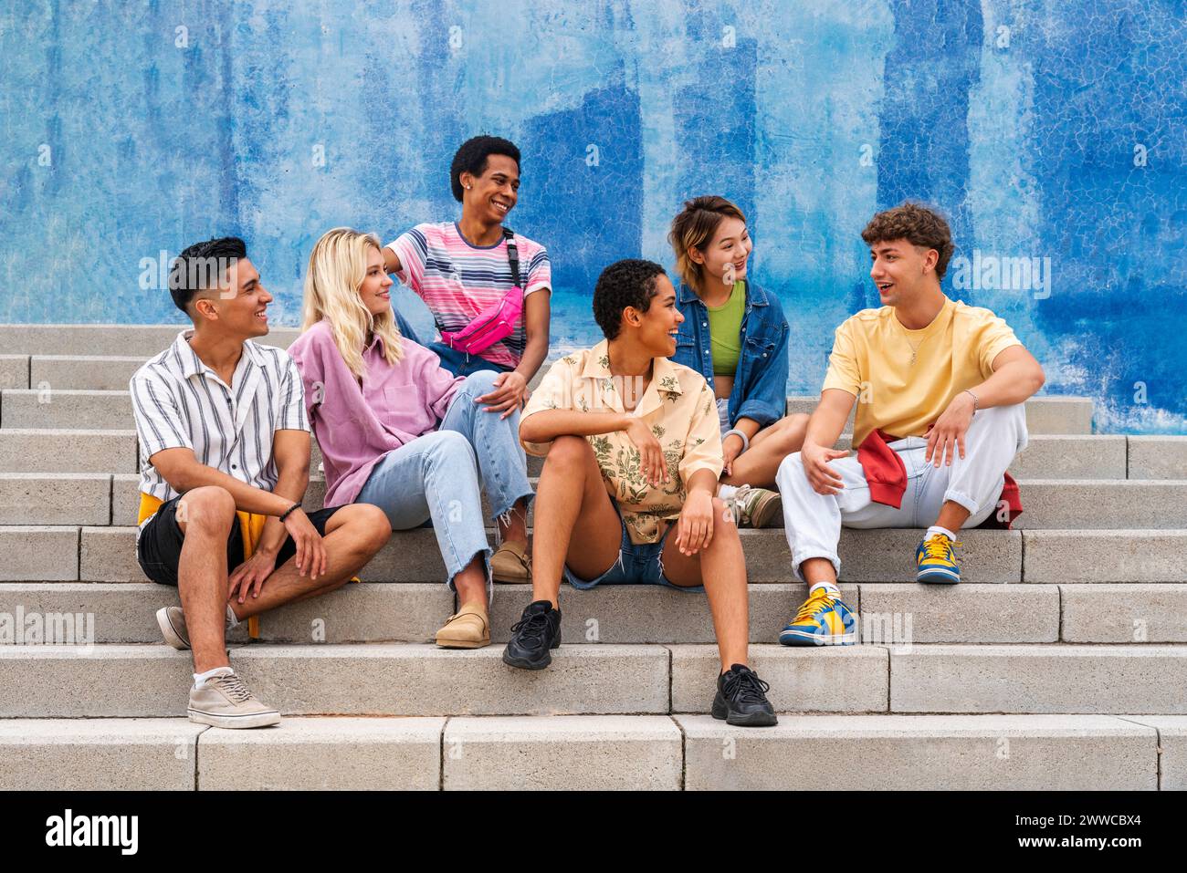 Groupe multiethnique de jeunes assis sur des marches devant le mur Banque D'Images