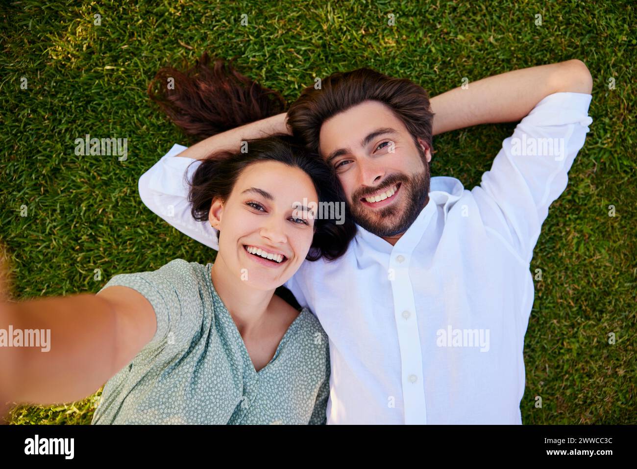 Jeune femme souriante prenant selfie avec un homme couché sur l'herbe Banque D'Images