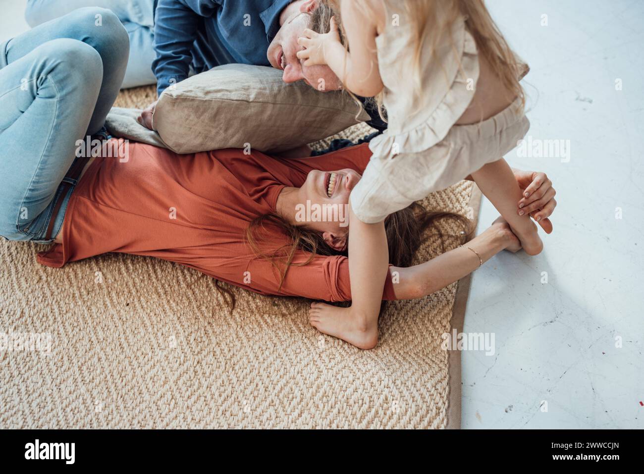 Mère et père joyeux jouant avec leur fille sur tapis à la maison Banque D'Images