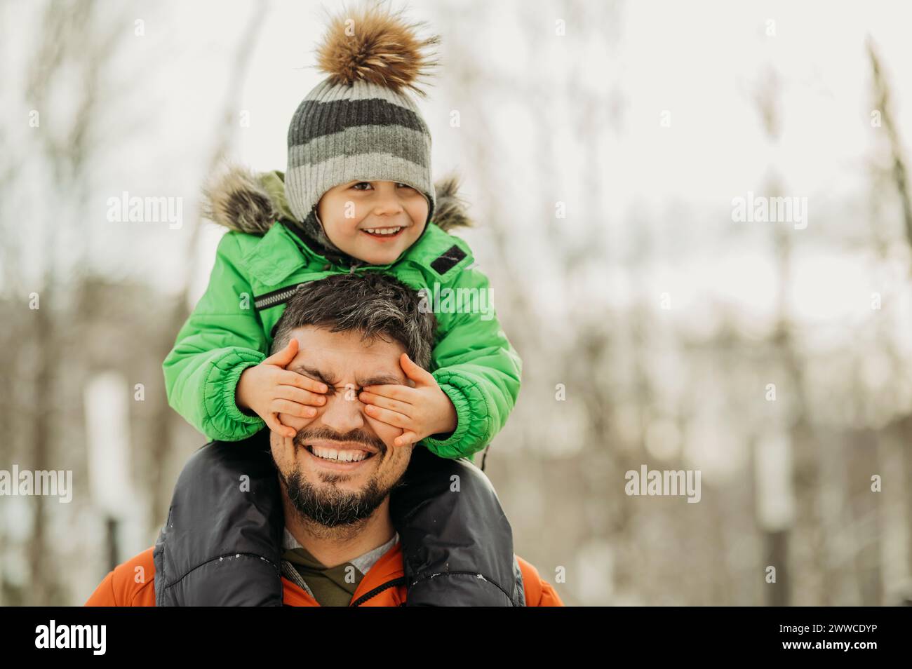Fils ludique couvrant les yeux du père avec les mains en hiver Banque D'Images