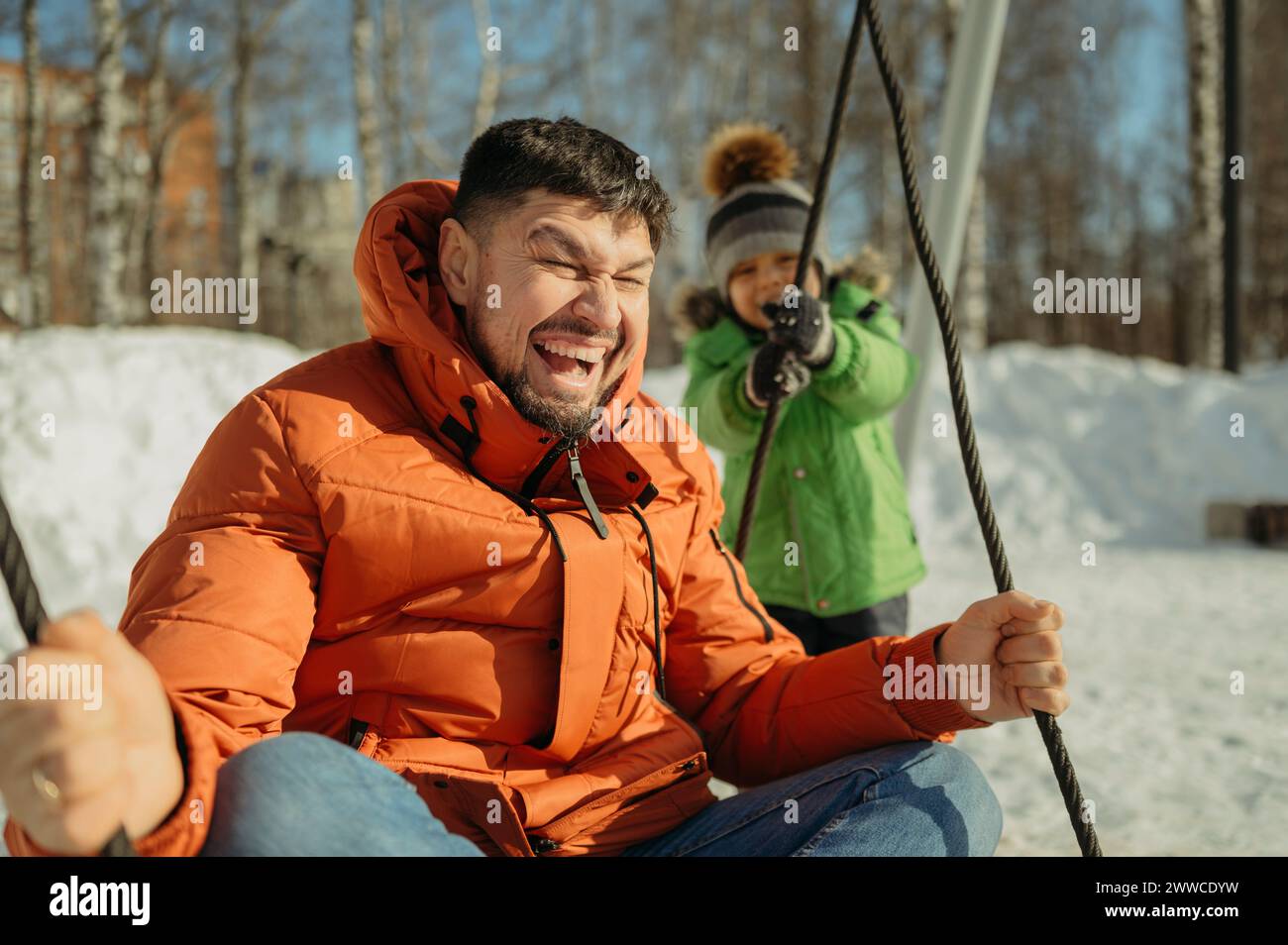 Père joyeux assis sur la balançoire avec son fils au parc Banque D'Images