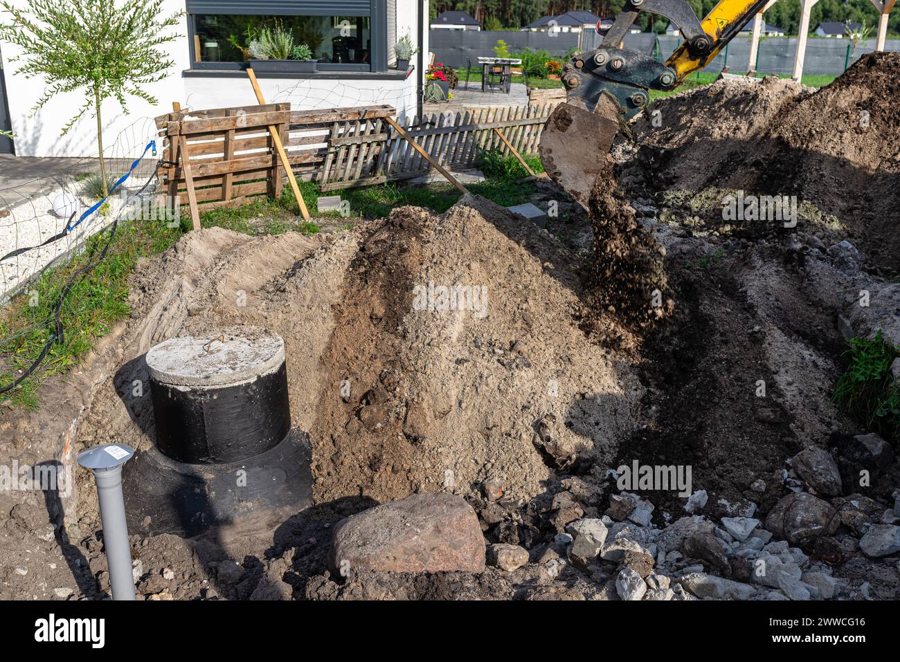 Utilisation d'une excavatrice pour enterrer une fosse septique en béton de 10 m3 située dans le jardin à côté de la maison. Banque D'Images