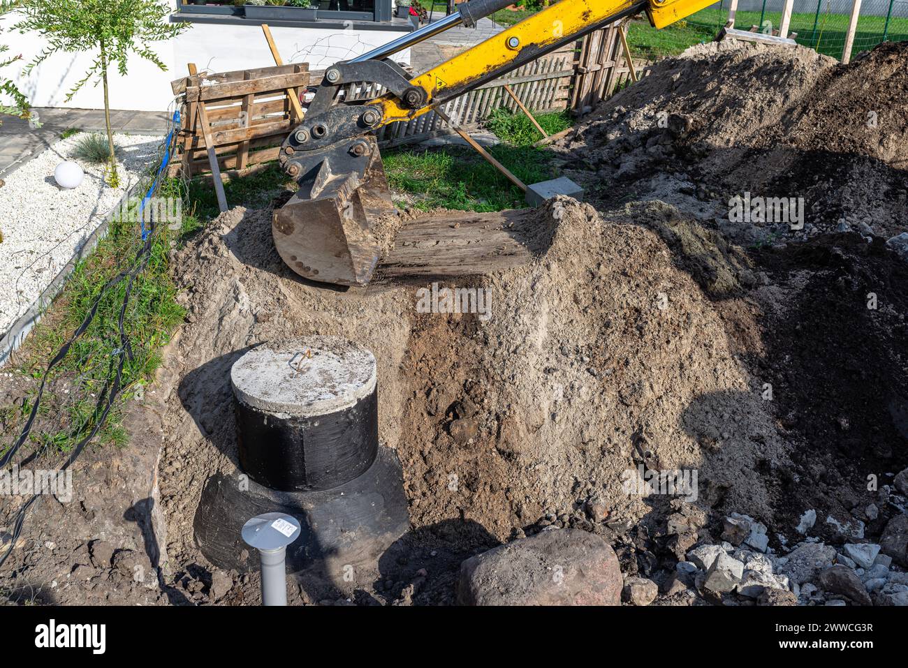 Utilisation d'une excavatrice pour enterrer une fosse septique en béton de 10 m3 située dans le jardin à côté de la maison. Banque D'Images