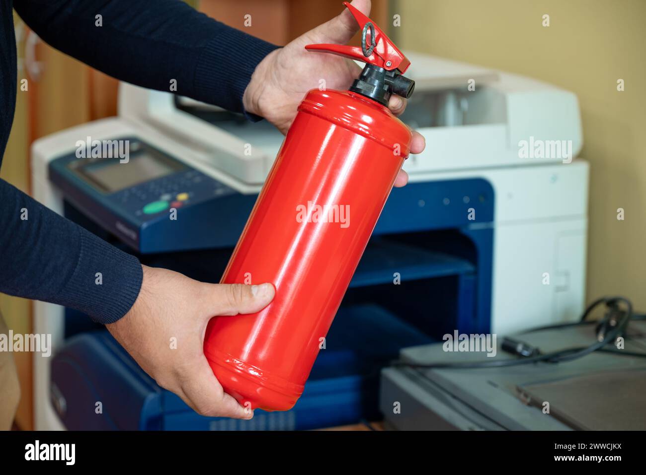 Un homme tient un extincteur dans ses mains sur fond d'équipement de bureau. Banque D'Images