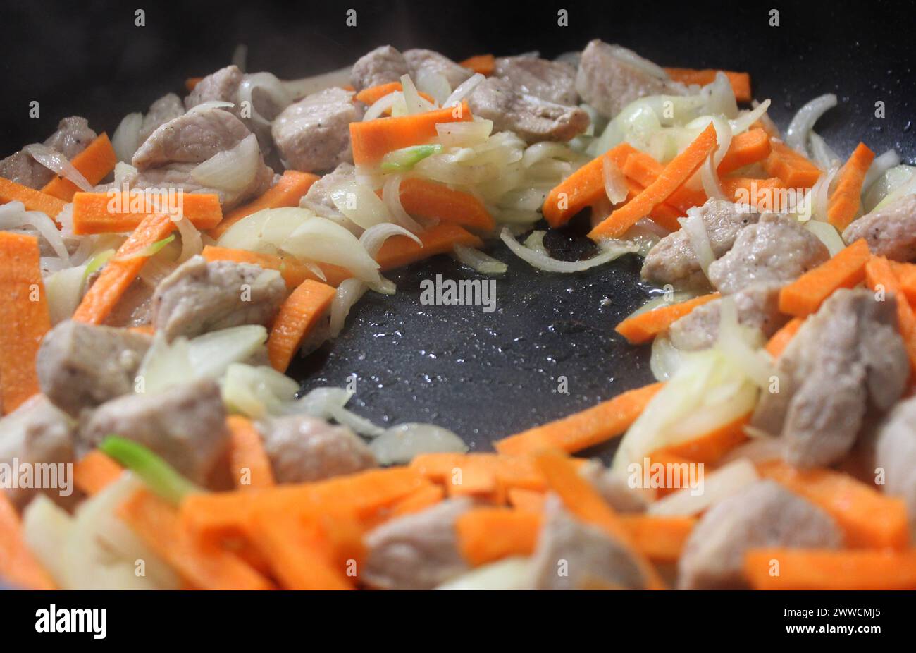 Morceaux de viande de porc, oignon et carotte cuits dans Une poêle avec de l'huile d'olive Banque D'Images