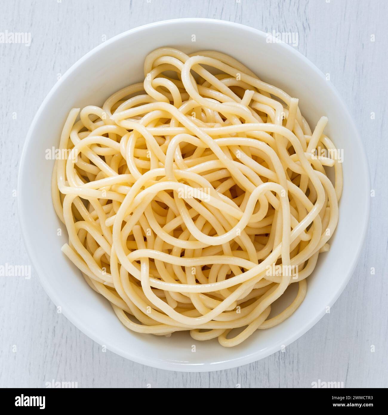 Spaghettis cuits dans un bol en céramique blanche isolé sur bois peint blanc. Vue de dessus. Banque D'Images