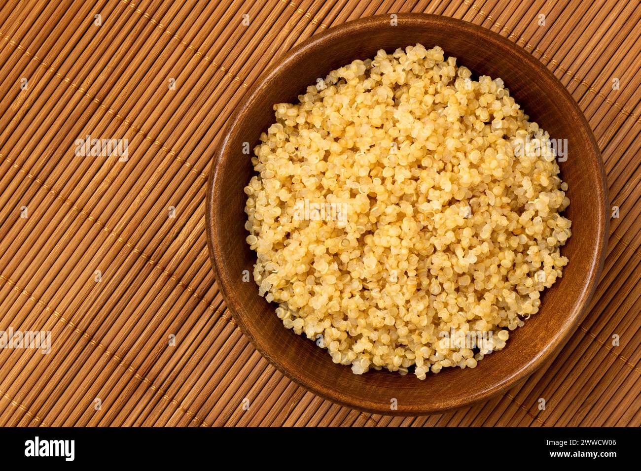 Quinoa blanc cuit dans un bol en bois foncé isolé sur bambou mat. Vue de dessus. Banque D'Images