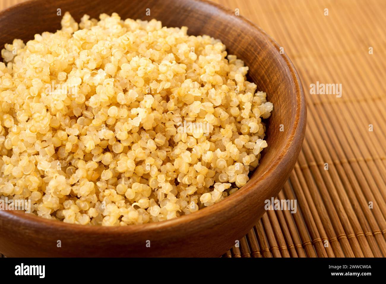 Détail de quinoa blanc cuit dans un bol en bois foncé sur bambou mat. Banque D'Images