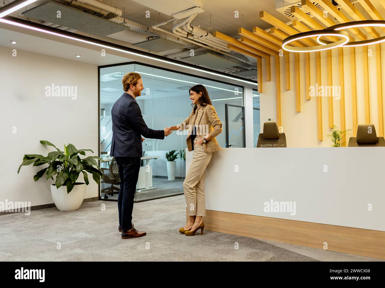 Deux professionnels échangeant des salutations avec une poignée de main amicale dans un environnement de bureau élégant Banque D'Images