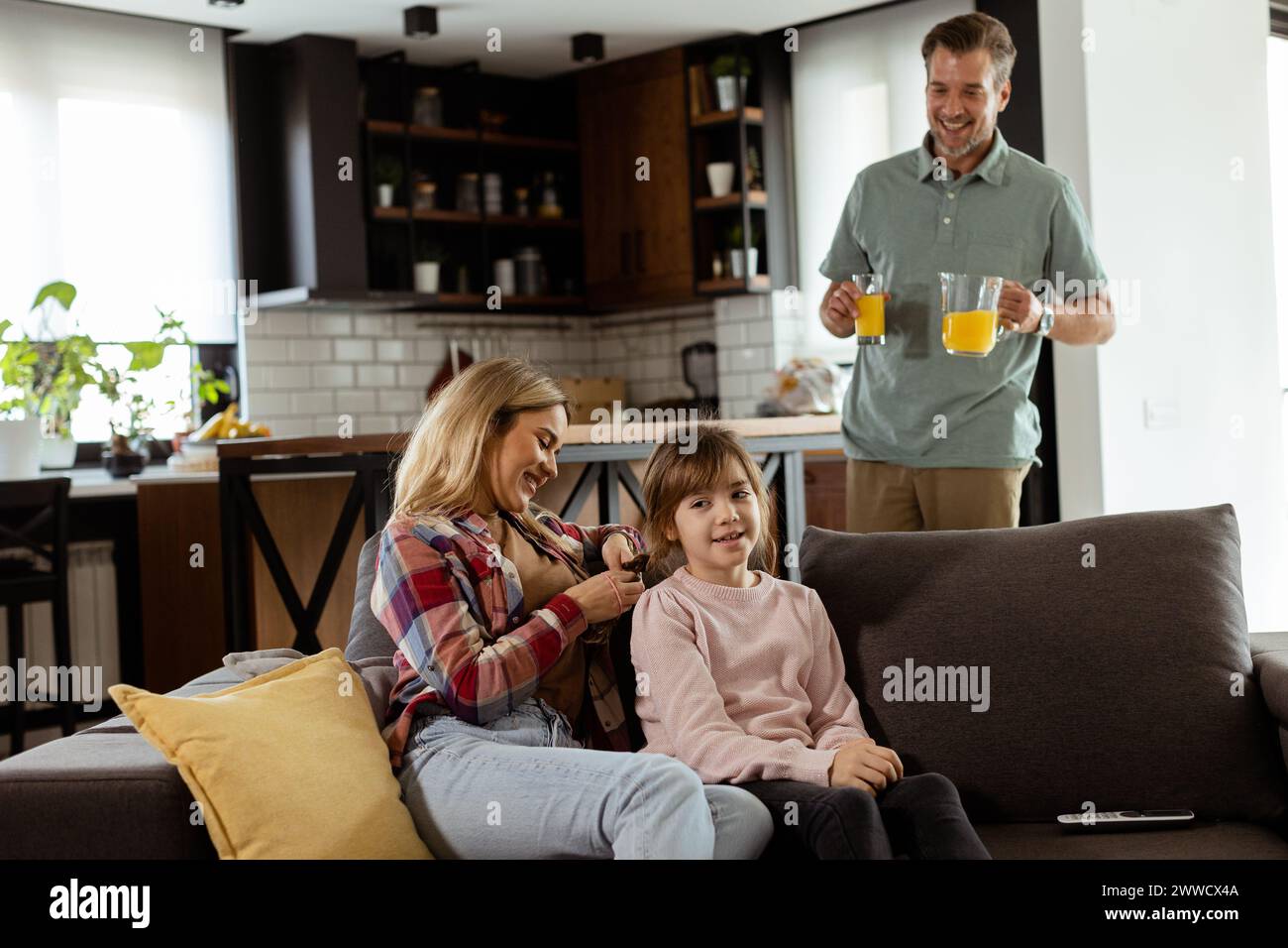 Un père souriant apporte un plateau de jus d'orange à sa famille heureuse assise dans un salon Banque D'Images