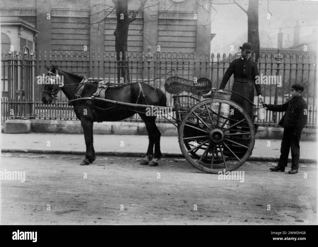 Description du Milkman : 'photographie d'un chariot à lait avec 'Devonshire Dairy' [10 Royal Hill, Greenwich] peint sur le côté, et un homme remettant une canette de lait à un garçon.' Photographie de RL Sirus. Date : 1884 sépia, lait, greenwich, transport, copy1 Banque D'Images