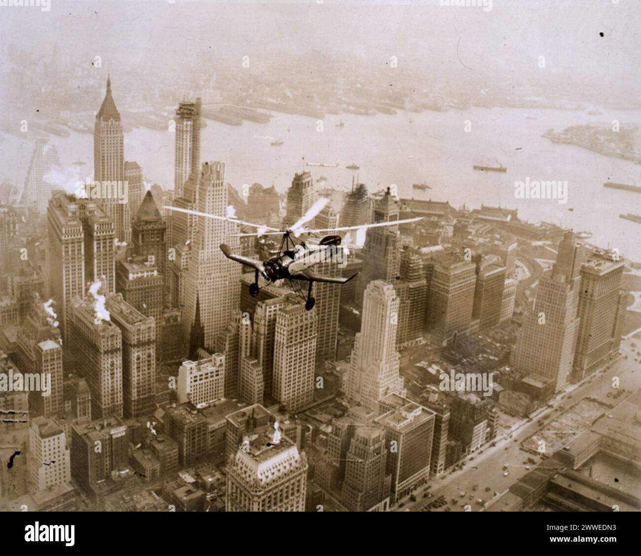 L'avenir est maintenant Description : une Cierva Autogiro de fabrication britannique survole l'île de Manhattan. Né de l'ingénieur aéronautique espagnol Juan de la Cierva, l'autogyre a été développé au début des années 1920 Le dossier des Archives nationales porte sur des propositions au sein de la Great Western Railway Company pour construire ce que l'on appellerait maintenant des hélistations dans les gares ferroviaires. Date : c.1931 newyorkcity, new york, amérique, gratte-ciel, états-unis, manhattan, avion, aviation, chemin de fer, autogyre, greatwesternrailway, autogiro, cierva, rotarywing, ciervaautogyro, ciervaautogiro Banque D'Images