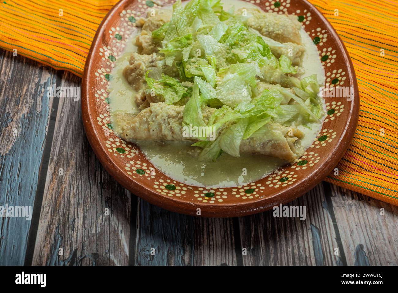 Enchiladas vertes avec de la laitue servie dans un plat en argile sur une table en bois. Banque D'Images