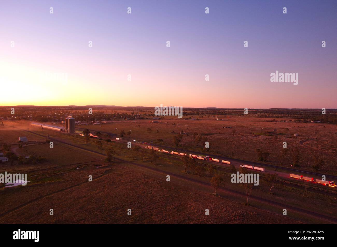 Aérien du coucher du soleil au-dessus de camions livrant du grain de blé au silo de Wallumbilla Queensland Australie Banque D'Images