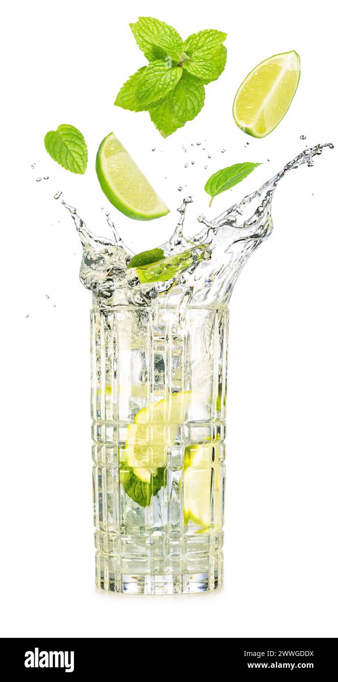 Quartiers de citron vert et feuilles de menthe tombant dans un verre débordant de cocktail de mojito isolé sur fond blanc. Banque D'Images