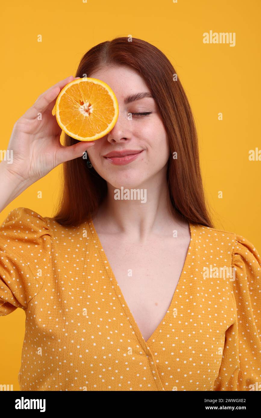 Belle femme couvrant l'oeil avec la moitié d'orange sur fond jaune Banque D'Images