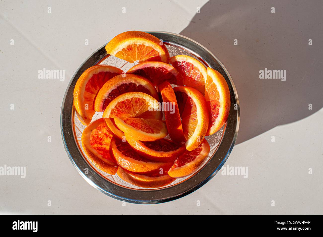 Un bol en verre rempli de tranches d'orange fraîches dans la lumière du soleil, par le haut Banque D'Images
