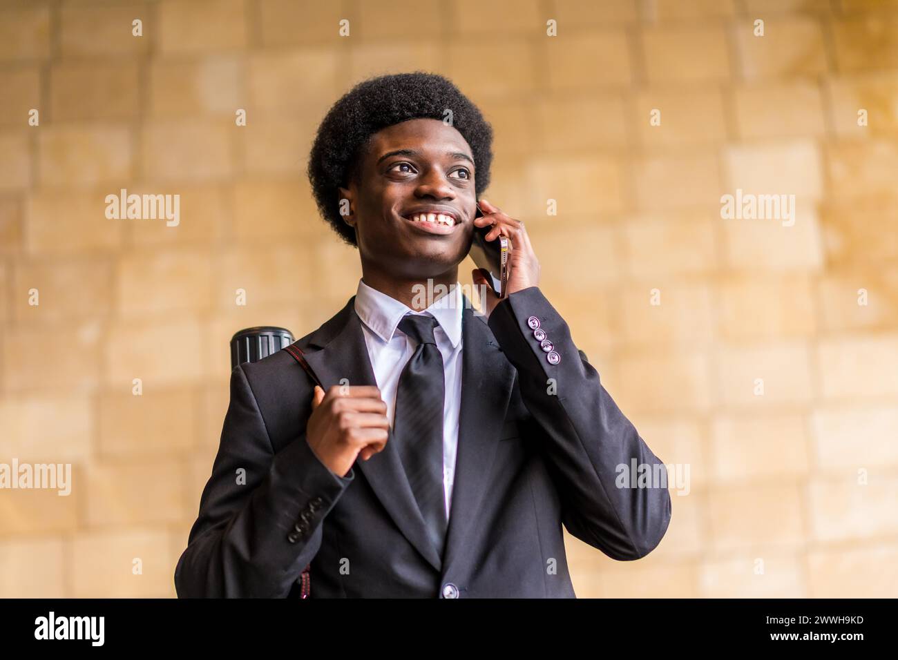 Portrait de vue à angle bas d'un jeune architecte africain fier parlant au mobile et souriant à l'extérieur Banque D'Images