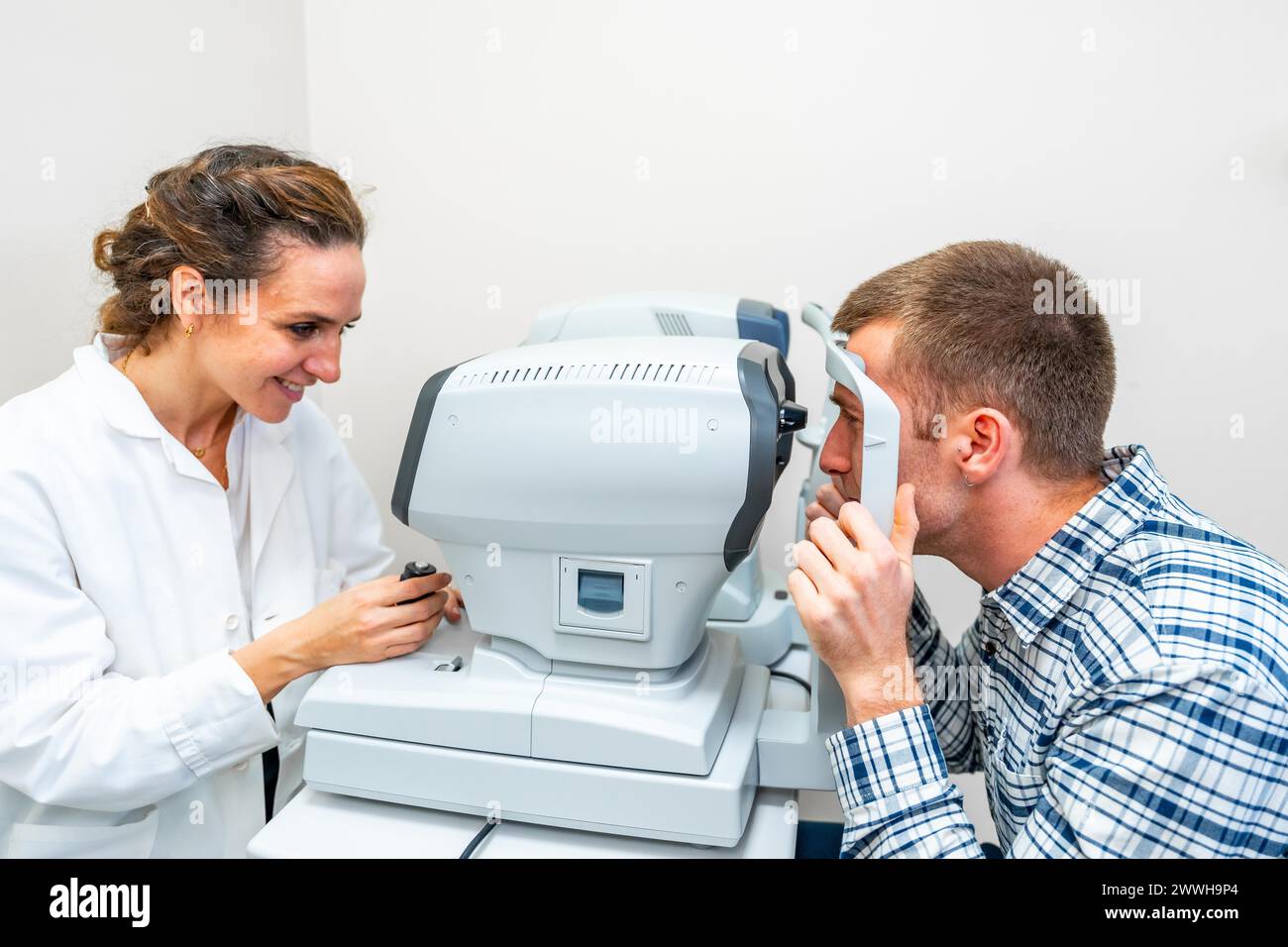 Vue de côté d'une ophtalmologiste scannant les yeux d'un homme en clinique Banque D'Images