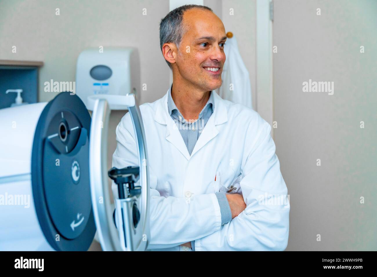 Fier ophtalmologiste masculin mature regardant distrait à côté d'une machine laser innovante dans une clinique Banque D'Images