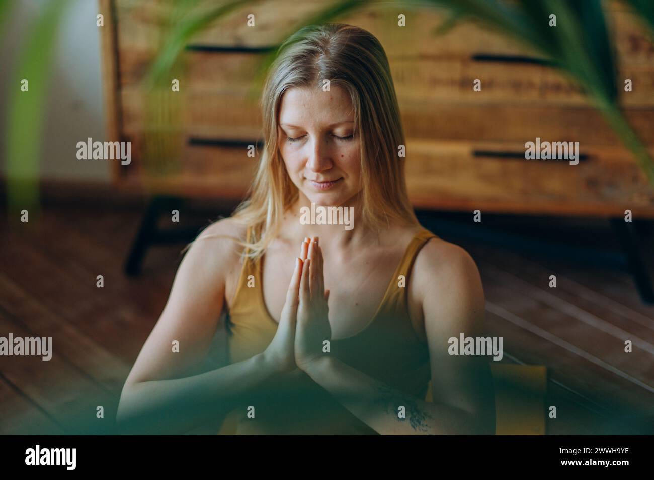 Une jeune femme dans une pose méditative, les mains en namaste, les yeux fermés en paix, avec une expression sereine, pratiquant le yoga dans un cadre intérieur tranquille. Pratique de la pleine conscience : femme méditant avec les mains dans la posture Namaste Banque D'Images