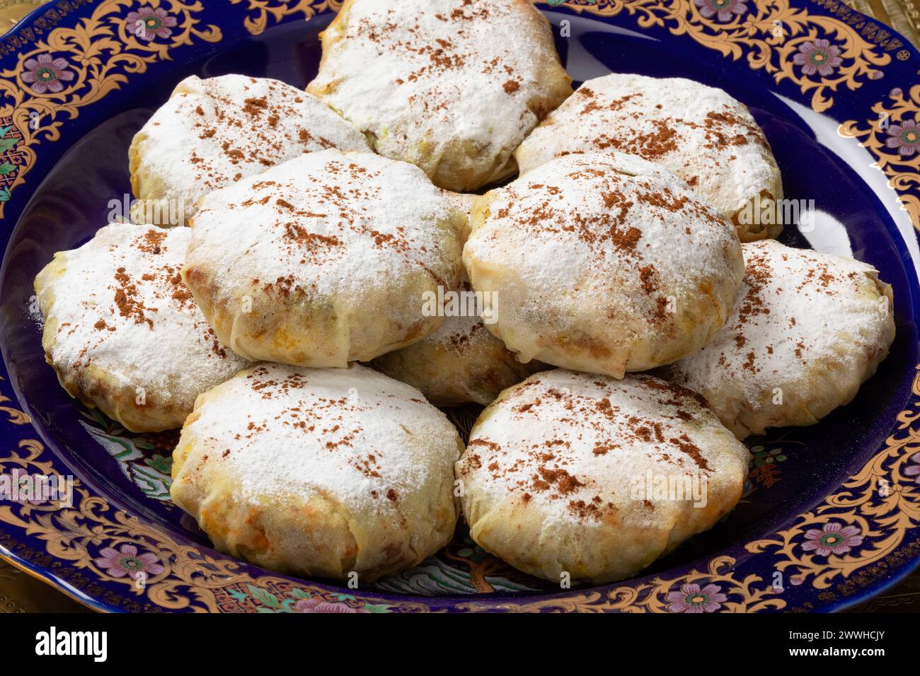 Assiette traditionnelle avec mini bastella marocaine fraîchement cuite farcie au poulet et recouverte de sucre et de cannelle gros plan Banque D'Images