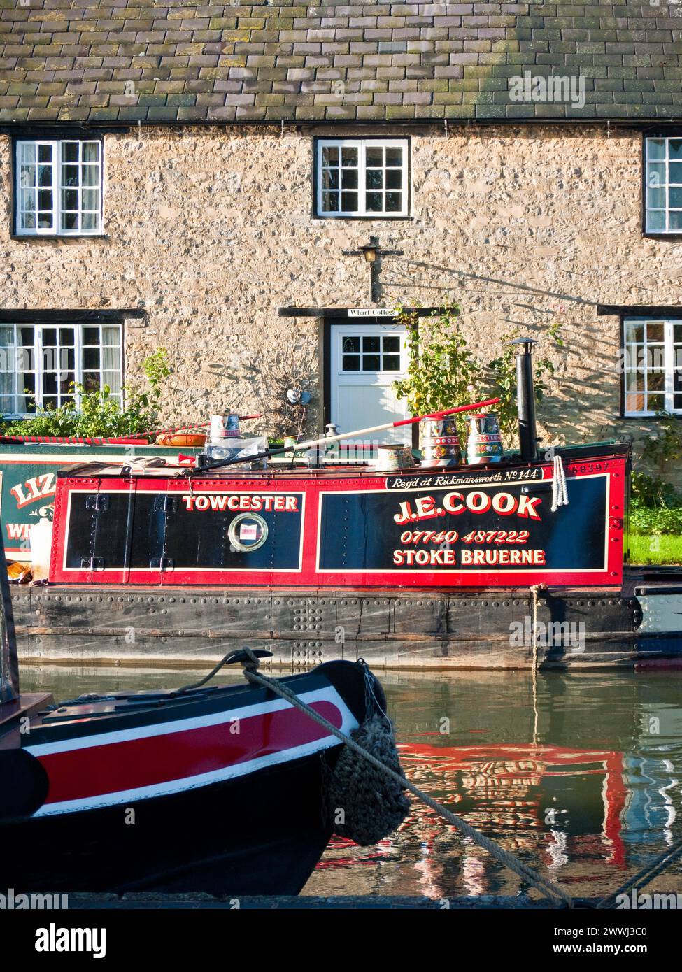 Vieux bateau de travail historique peint de couleurs vives amarré à l'extérieur d'un chalet au bord d'un canal sur le Grand Union canal à Stoke Bruerne, Angleterre, Royaume-Uni, Grande-Bretagne, Northa Banque D'Images