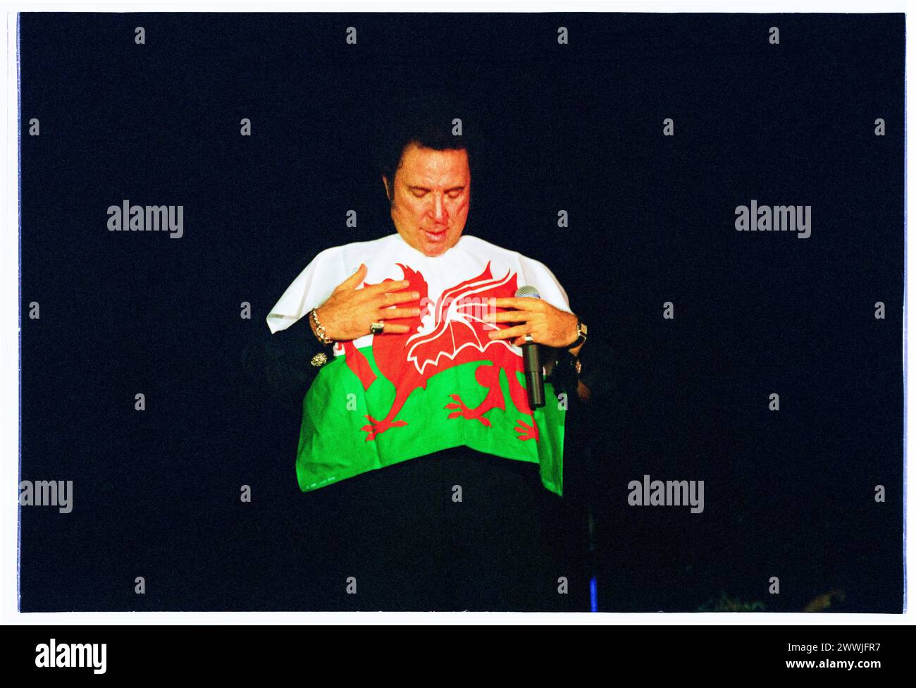 TOM JONES, CONCERT À DOMICILE, DRAPEAU GALLOIS, 2000 : TOM JONES, légende du chant gallois de 60 ans, pose avec un drapeau gallois jeté par la foule en direct à Cardiff International Arena CIA à Cardiff, pays de Galles, Royaume-Uni le 9 novembre 2000. Photo : Rob Watkins. INFO : Tom Jones, né en 1940 au pays de Galles, est un chanteur gallois légendaire connu pour sa voix puissante et sa présence dynamique sur scène. Avec des tubes intemporels comme « It's Not Unusual » et « Delilah », Jones a connu une carrière prolifique couvrant plusieurs genres, consolidant son statut d'artiste emblématique. Banque D'Images