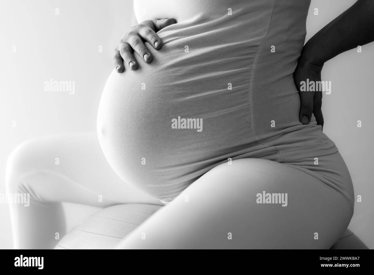 Description : femme enceinte avec bosse de bébé lourdement enceinte assise sur la balle de gymnastique traite les maux de dos et tient la main sur son dos douloureux. Vue latérale. Blanc b Banque D'Images