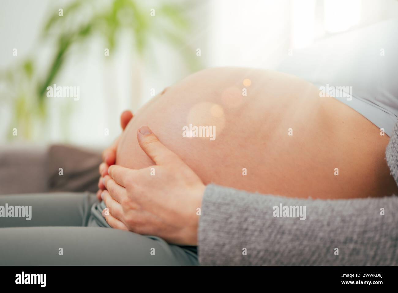 Description : vue à angle bas de la femme dans les derniers mois de grossesse tenant doucement son ventre rond. Grossesse troisième trimestre - semaine 34. Vue latérale. Ensoleillé Banque D'Images