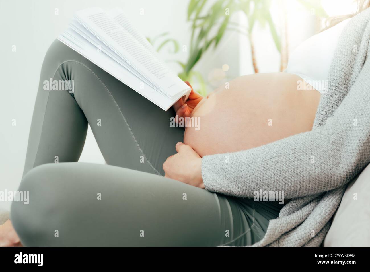 Description : vue de côté de la femme dans les derniers mois de grossesse tenant doucement son ventre tout en lisant un livre. Grossesse troisième trimestre - semaine 34 Banque D'Images