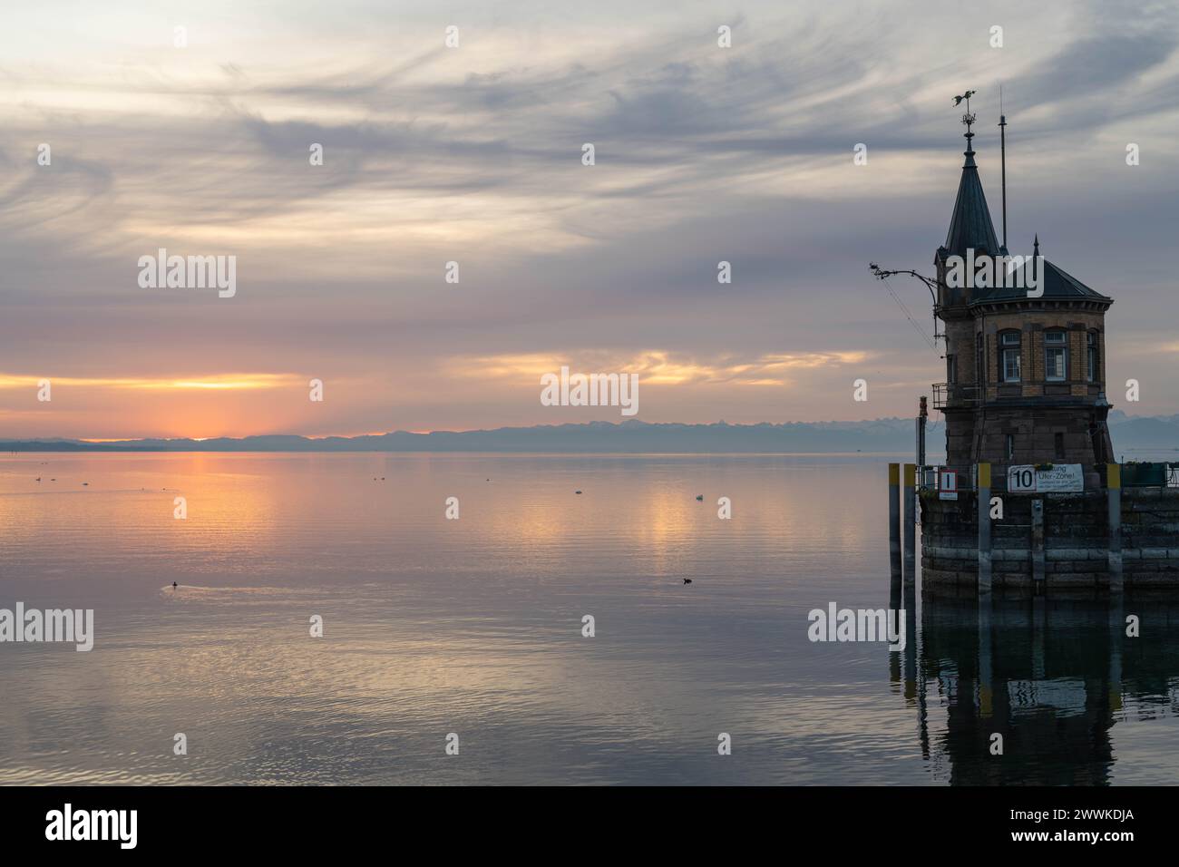 Beschreibung : Der Leuchtturm an der Hafeneinfahrt mit dem ruhigen See und den Bergen am Horizont in der Morgendämmerung. Konstanz, Bodensee, Bade-Wür Banque D'Images