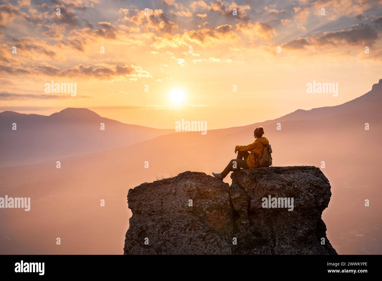 Serene femme randonneur est assis et se détendre sur le grand rocher contre le coucher du soleil dans les montagnes Banque D'Images