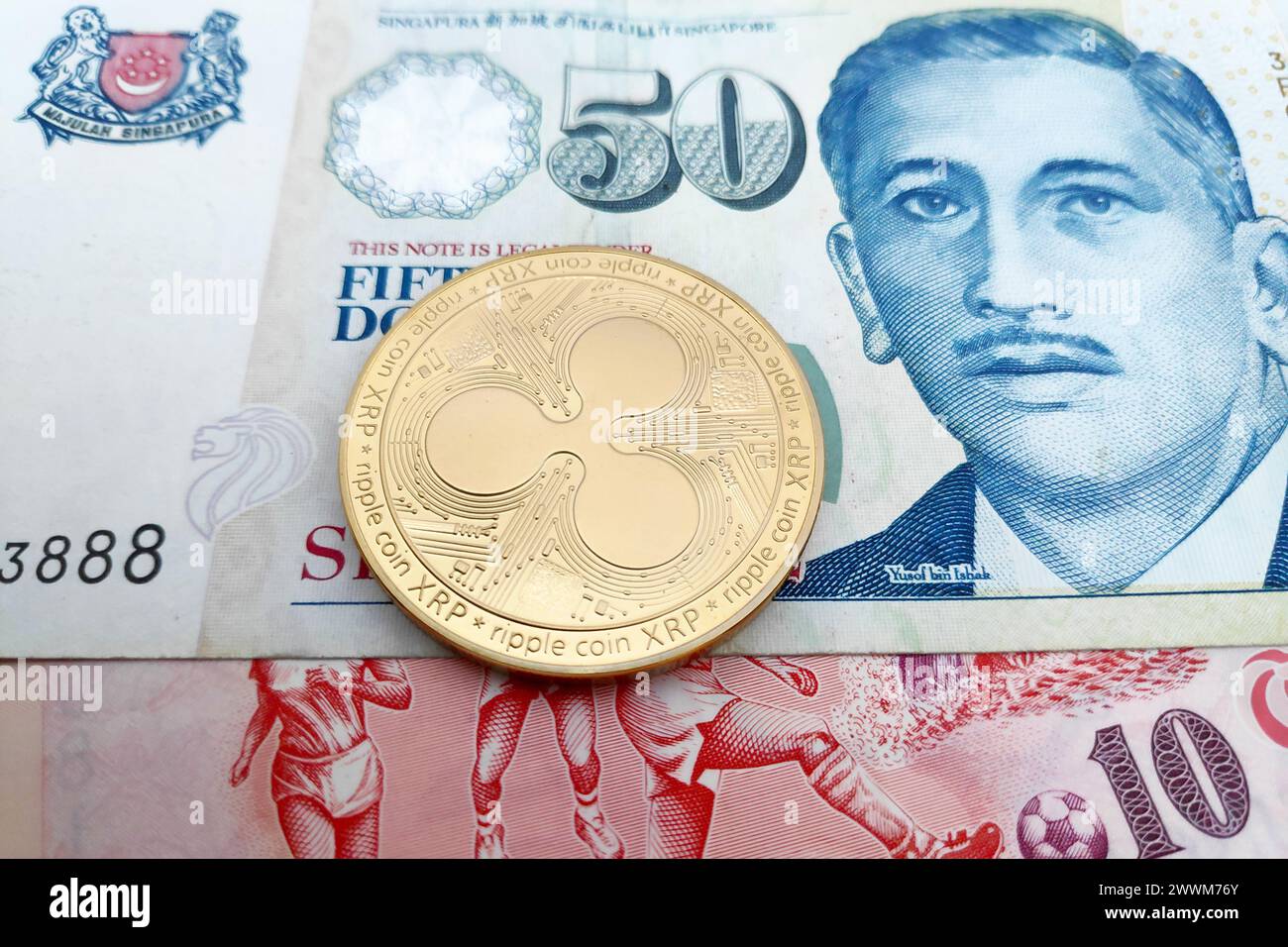 Gros plan sur une pièce de monnaie Ripple dorée au-dessus d'une pile de billets de Dollar singapourien. Banque D'Images