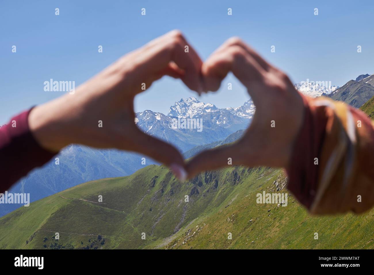 Deux mains créent une forme de cœur, capturant une vue de montagnes enneigées au loin Banque D'Images