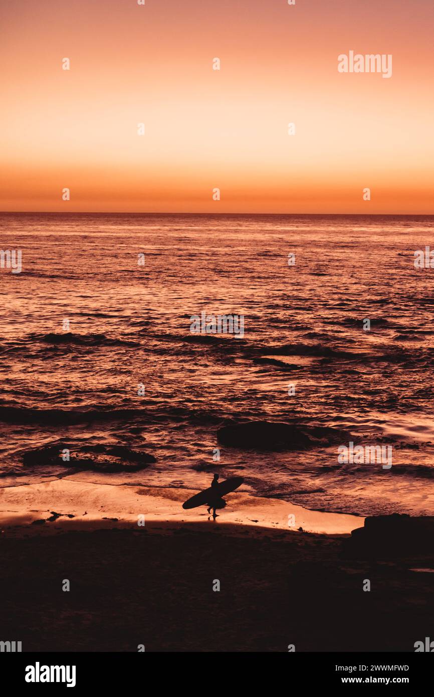 Silhouette de surfeur marchant sur la plage au crépuscule Banque D'Images