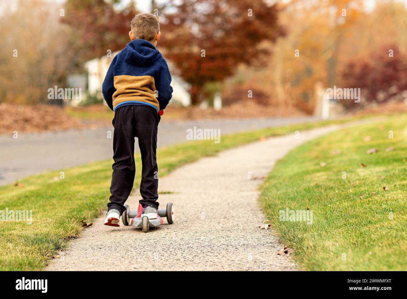 Garçon chevauchant scooter sur les trottoirs du quartier à l'automne Banque D'Images