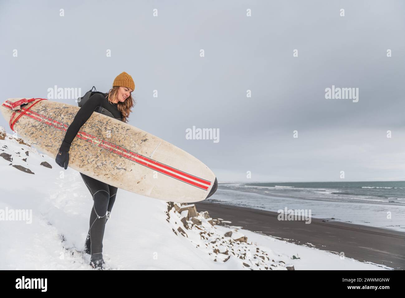 Femme marchant sur la plage avec planche de surf hiver islande Banque D'Images