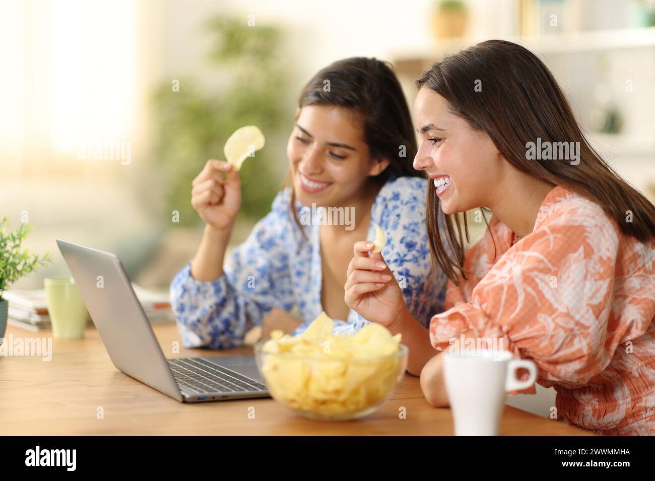 Deux femmes à la maison mangeant des bateaux de pommes de terre regardant le film sur ordinateur portable Banque D'Images