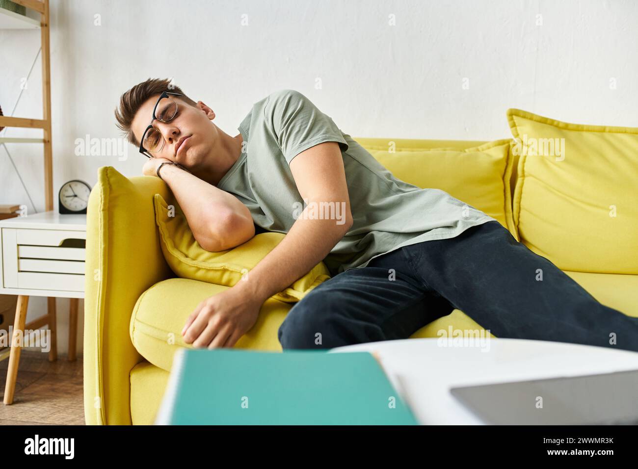 jeune étudiant fatigué avec des cheveux bruns et des lunettes de vision dormant sur un canapé jaune dans le salon Banque D'Images