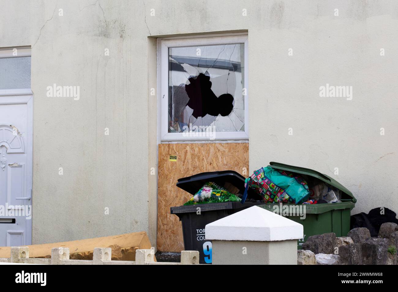 Fenêtre brisée à l'extérieur de la façade d'une maison résidentielle avec beaucoup de déchets dehors Banque D'Images