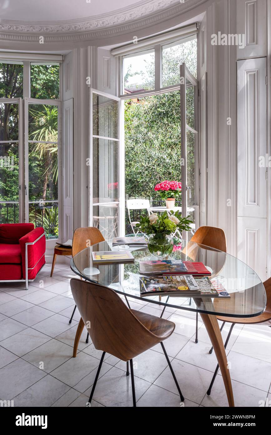 Fauteuil vintage avec table et chaises à portes françaises ouvertes dans un appartement moderne de l'ouest de Londres, Royaume-Uni Banque D'Images