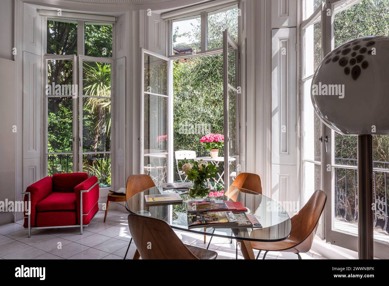 Fauteuil vintage avec table et chaises à portes françaises ouvertes dans un appartement moderne de l'ouest de Londres, Royaume-Uni Banque D'Images