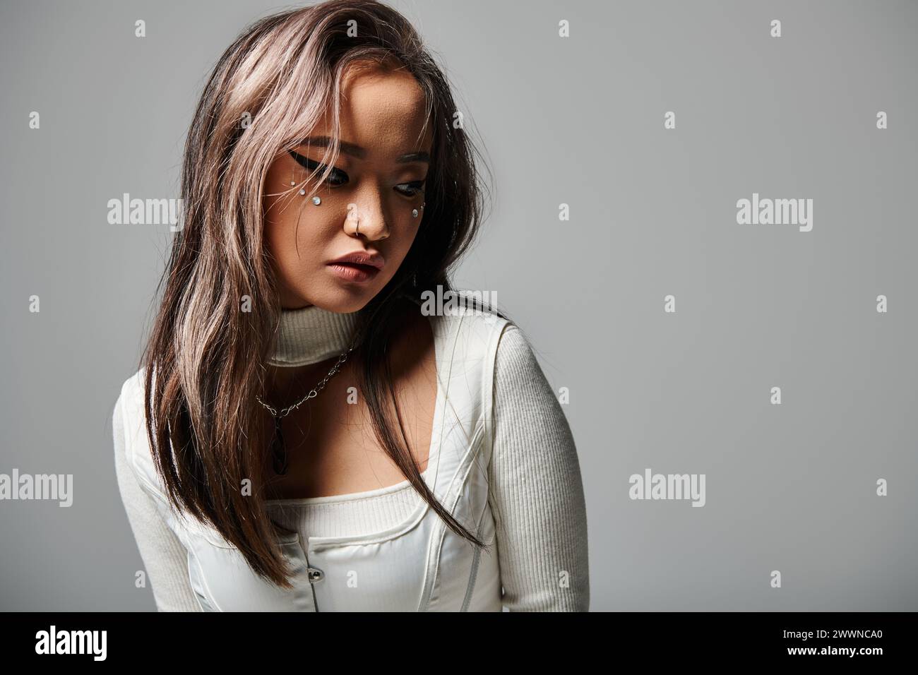 charmante jeune femme couvrant le visage avec des cheveux et regardant de côté sur fond gris Banque D'Images