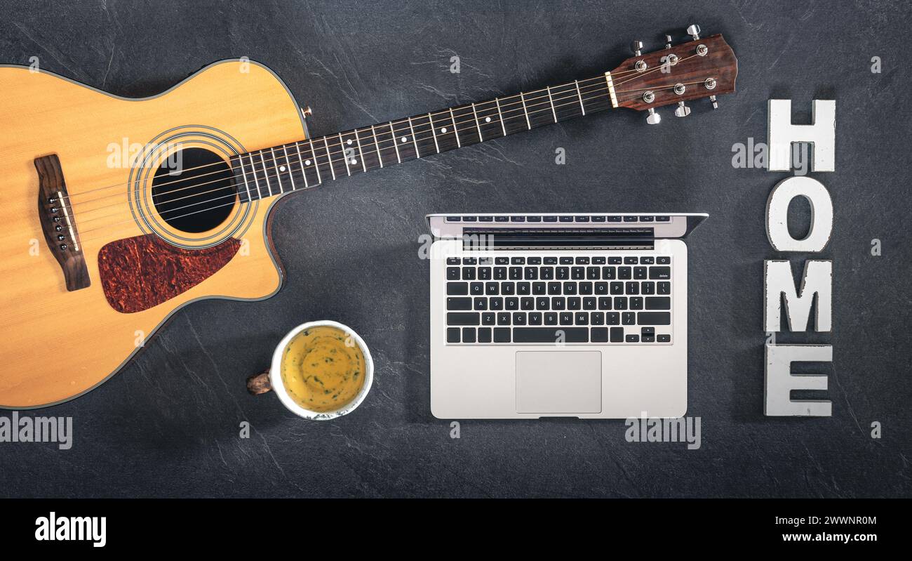 Ordinateur portable, guitare acoustique et une tasse de thé sur fond noir, vue de dessus. Banque D'Images