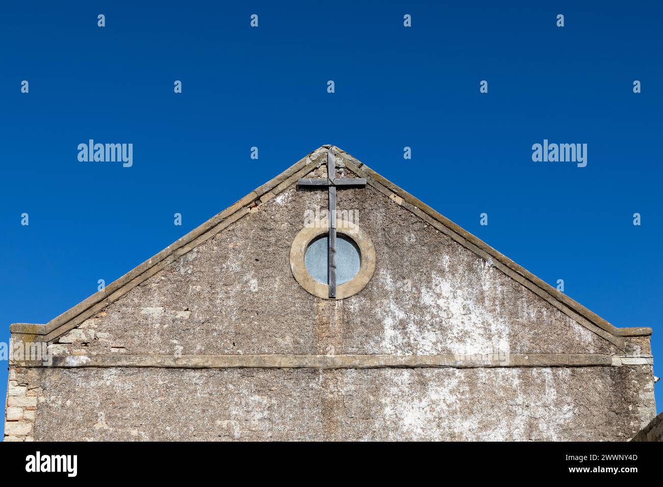 Extrémité de pignon d'une ancienne église abandonnée avec une fenêtre circulaire et une croix en bois attachée au mur. Banque D'Images