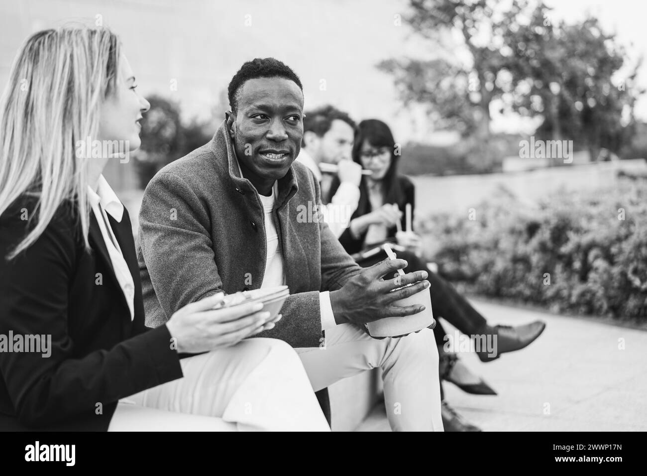 Collègues multiraciaux mangeant ensemble en plein air dans un parc de la ville pendant la pause luch - diversité et concept d'emploi - édition noir et blanc - Focus sur l'afrique Banque D'Images