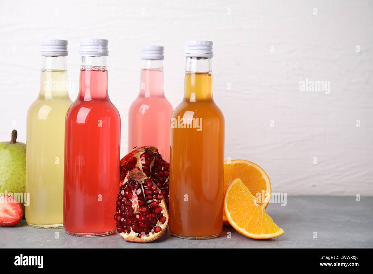 Délicieux kombucha dans des bouteilles en verre et des fruits frais sur une table grise sur fond blanc Banque D'Images
