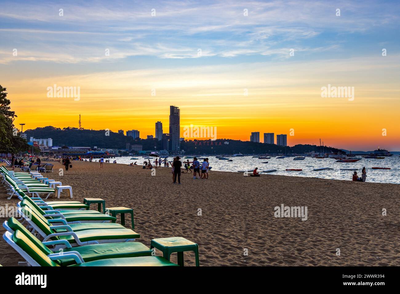 Paysage de plage de Pattaya avec sable, chaises longues, bâtiments, personnes et horizon au coucher du soleil, Thaïlande Banque D'Images